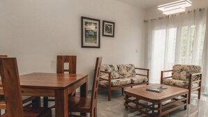 A dining area with wooden furniture, a sofa with a leaf pattern, and two framed pictures on the wall.