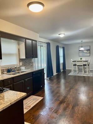 A modern kitchen with dark wood flooring, a built-in dishwasher, and a dining area with a table and chairs. - Dream Getaway Home in Snellville, Front Yard, Deck and Smart TVs in Every Room! (Snellville)