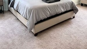 Un dormitorio con cama, ventilador de techo, mesita de noche, lámpara y un cuadro en la pared.