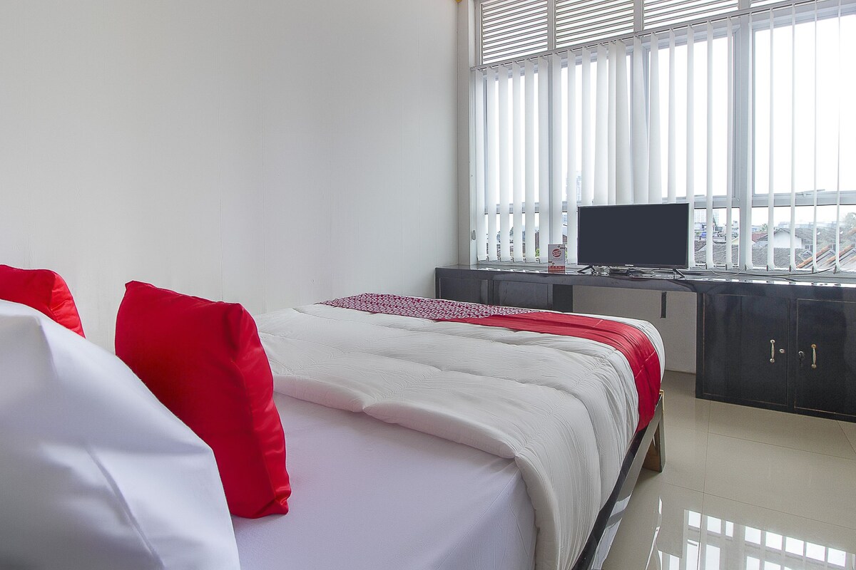 A bedroom with a bed, a TV, and a window with blinds.
