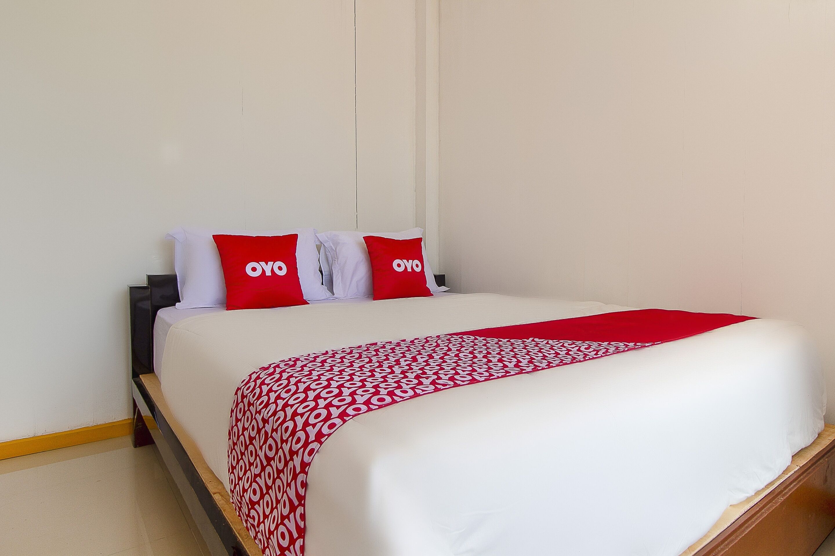 Cama bem arrumada com roupa de cama branca e vermelha, incluindo travesseiros com o logotipo "OYO".