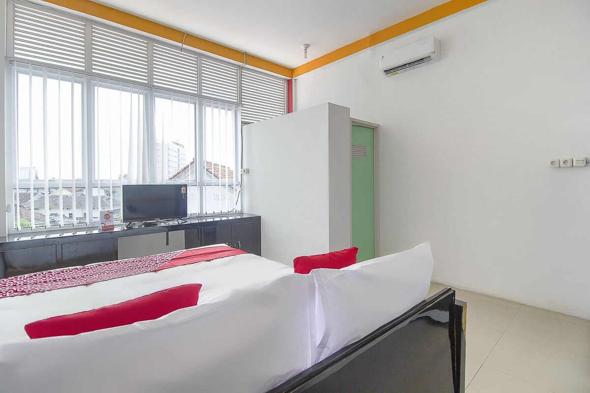 Una habitación de hotel con una cama, un escritorio con una computadora, una ventana con persianas y una puerta.