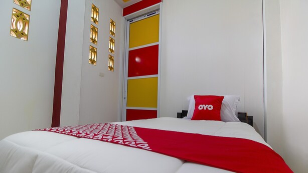 Una habitación de hotel con una cama, una colcha roja y blanca, y un almohadón rojo con el logotipo 'OYO'.