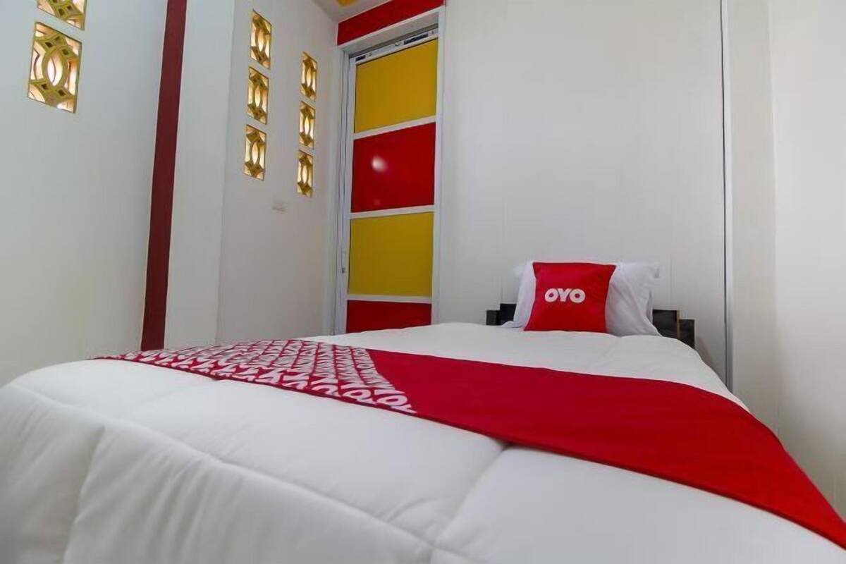 A hotel room with a bed, a red and white bedspread, and a red pillow with "OVO" on it.