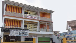 Un edificio de varios pisos con un cartel que dice 'Restu Inn Penginapan' y otro cartel que dice 'Toko Keramik Restu Ibu'.