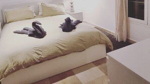Ein Schlafzimmer mit einem Bett, Kissen, einem Nachttisch, einer Lampe und einem Fenster mit Vorhängen.