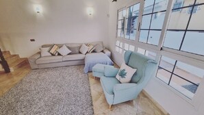 Ein Wohnzimmer mit einem beigefarbenen Sofa, einem blauen Sessel und einem gemusterten Teppich.