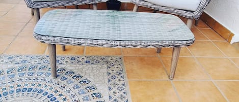 Un sofá de mimbre con cojines a rayas, una mesita y una planta en maceta.