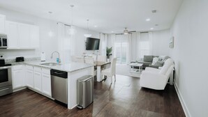 Une cuisine moderne avec des meubles blancs, un îlot central et un coin repas comprenant une table et des chaises blanches.