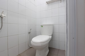 A small, white-tiled bathroom with a toilet, a showerhead, and a towel rack. - OYO 92166 Nirwana Inn Syariah (Sewon)
