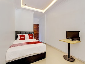 A modern hotel room with a bed, a TV on a stand, and a wooden door. - OYO 92166 Nirwana Inn Syariah (Sewon)