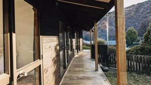 A covered wooden deck with large windows and a view of a mountainous landscape. - Charming House With all the Home Comforts (Arrowtown)