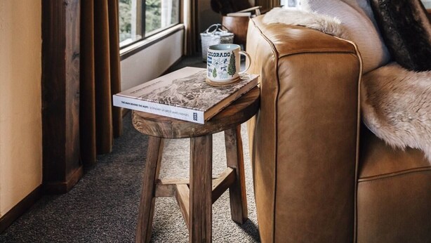 A cozy room with a wooden ceiling, a leather sofa, a table with a mug, and large windows offering a view of the outdoors. - Charming House With all the Home Comforts (Arrowtown)