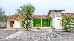 A house with a tiled roof, a green wall, and a paved courtyard with hexagonal tiles. - Hotel O Sari Laut (Temon)