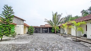 A courtyard with hexagonal paving, palm trees, and buildings with red-tiled roofs. - Hotel O Sari Laut (Temon)