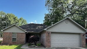 A two-story house with a garage, brick exterior, and a small front yard with grass and flowers. - Life is Good in Mayflower (Mayflower)