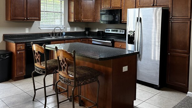 A kitchen with wooden cabinets, a stainless steel refrigerator, a microwave, and a granite countertop. - Life is Good in Mayflower (Mayflower)