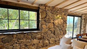 A stone wall, a window, and a beige sofa with pillows.