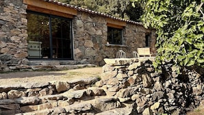 A stone building with a tiled roof, large windows, and a stone staircase leading to a patio area.