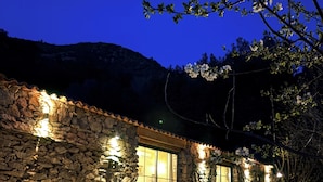A stone building with a large glass door, outdoor seating, and a stone wall.