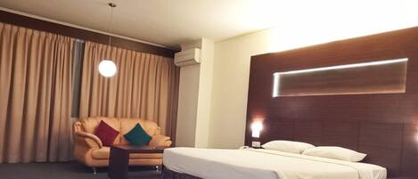 A hotel room with a bed, a sofa, a small table, and a hanging light fixture.