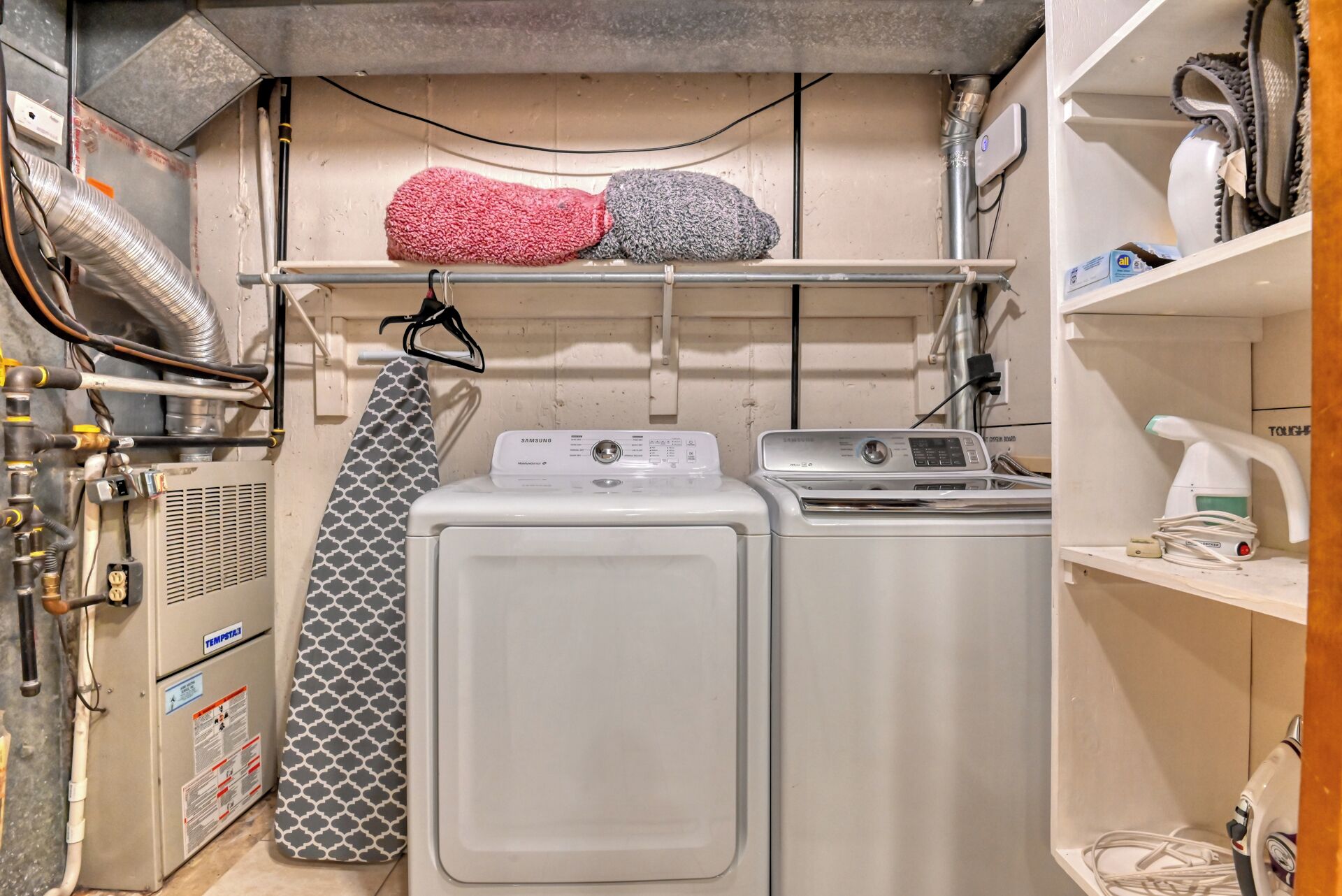 A compact laundry area with two washing machines, a drying rack, and a water heater.