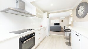 Uma cozinha moderna com armários brancos, forno embutido, coifa de aço inoxidável e um relógio de parede grande.