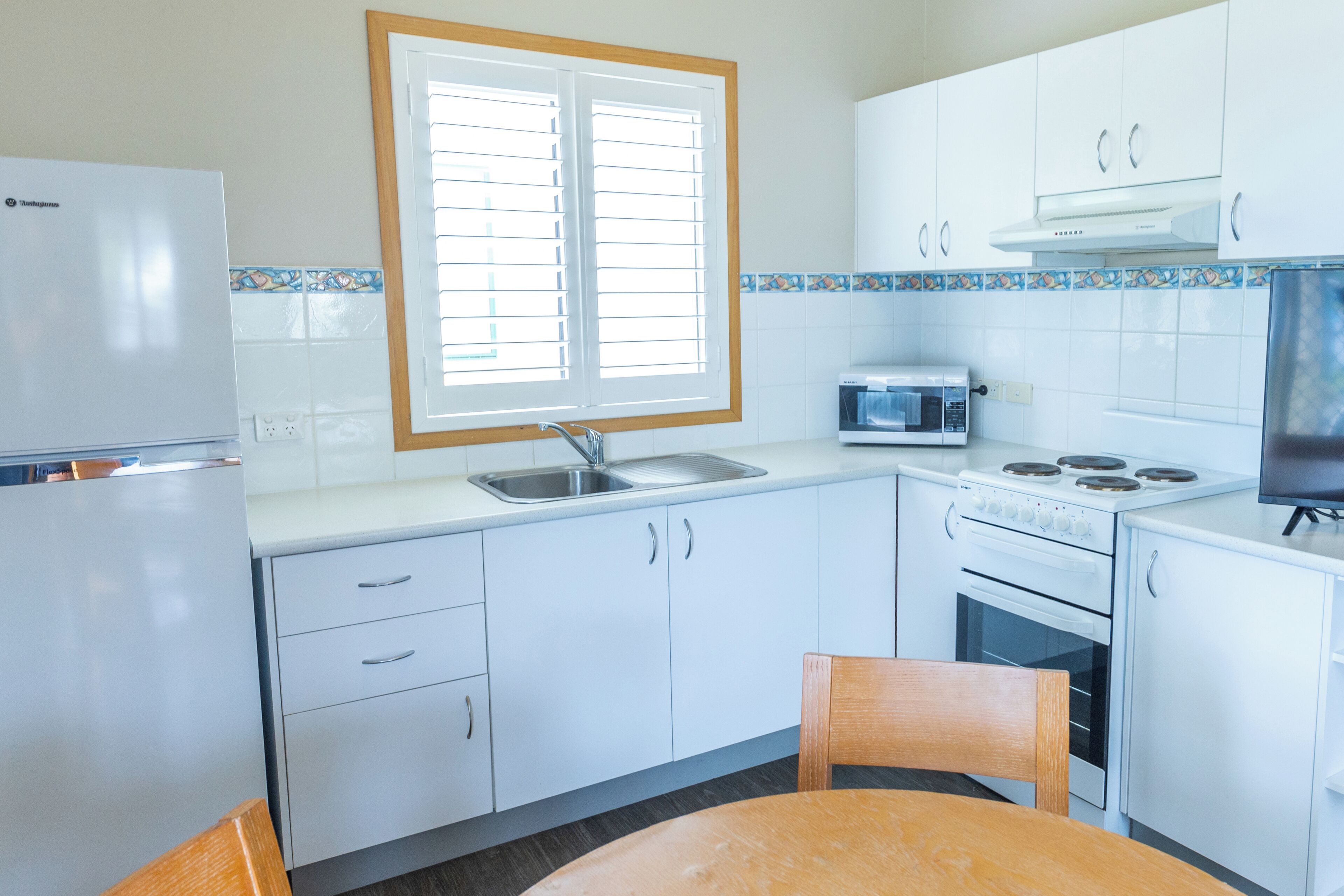 Una cocina compacta con armarios blancos, microondas, estufa y refrigerador.