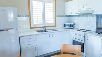 Una cocina compacta con armarios blancos, microondas, estufa y refrigerador.