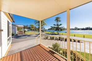 A covered outdoor area with a wooden deck, a view of a lake, and a pathway leading to a building. - NRMA Forster Tuncurry Holiday Park (Tuncurry)