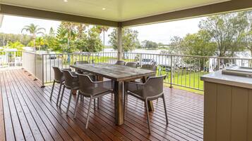 Un espace extérieur abrité, doté d’une terrasse en bois, d’une table avec des chaises et offrant une vue sur une étendue d’eau et la verdure.