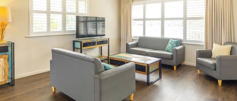 A living room with a sofa, armchair, coffee table, and a television on a stand.