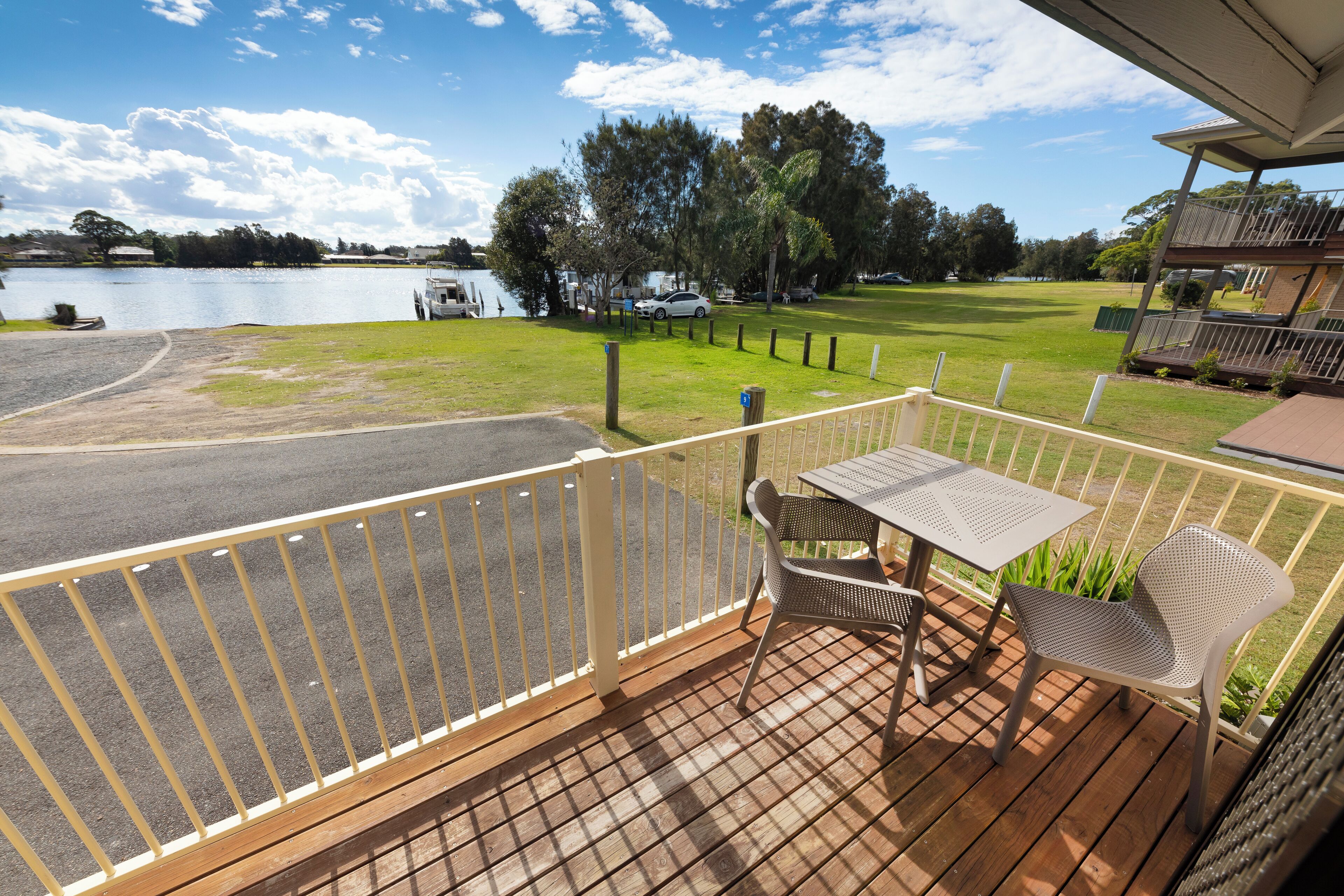 Une terrasse avec une table et des chaises donnant sur un lac, d’où l’on aperçoit un terrain de golf et des véhicules garés au loin.