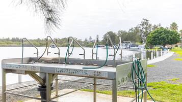 Uma estação portátil de água com várias torneiras e mangueiras, próxima a um corpo de água com barcos e vegetação ao fundo.