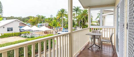 A wooden deck with a table and chairs, overlooking a parking area and buildings with palm trees.