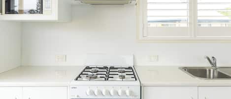 Een moderne keuken met witte kasten, een ingebouwde magnetron, een gasfornuis en een raam met jaloezieën.