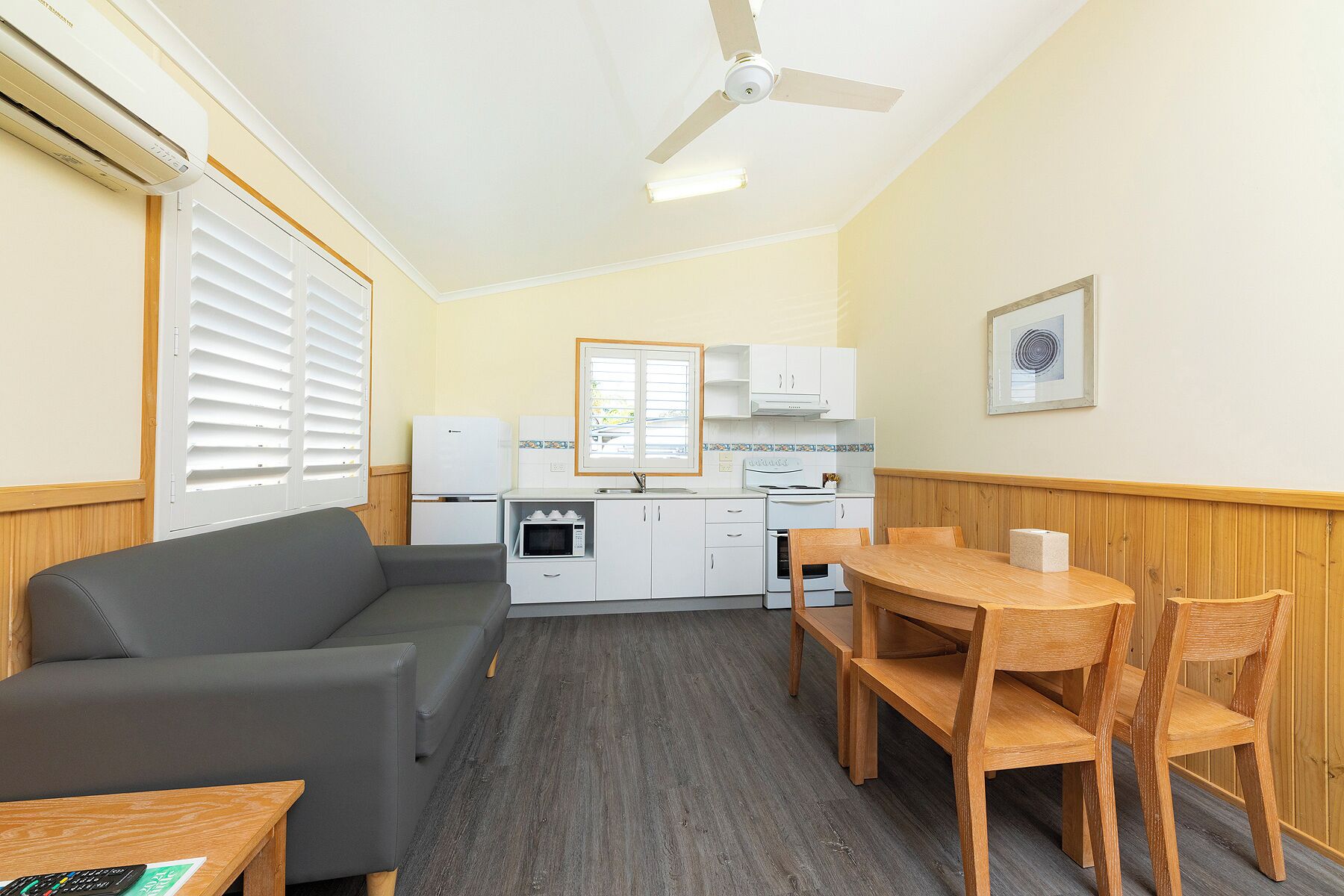 A compact living space with a sofa, a dining table with chairs, a kitchenette, and a ceiling fan.