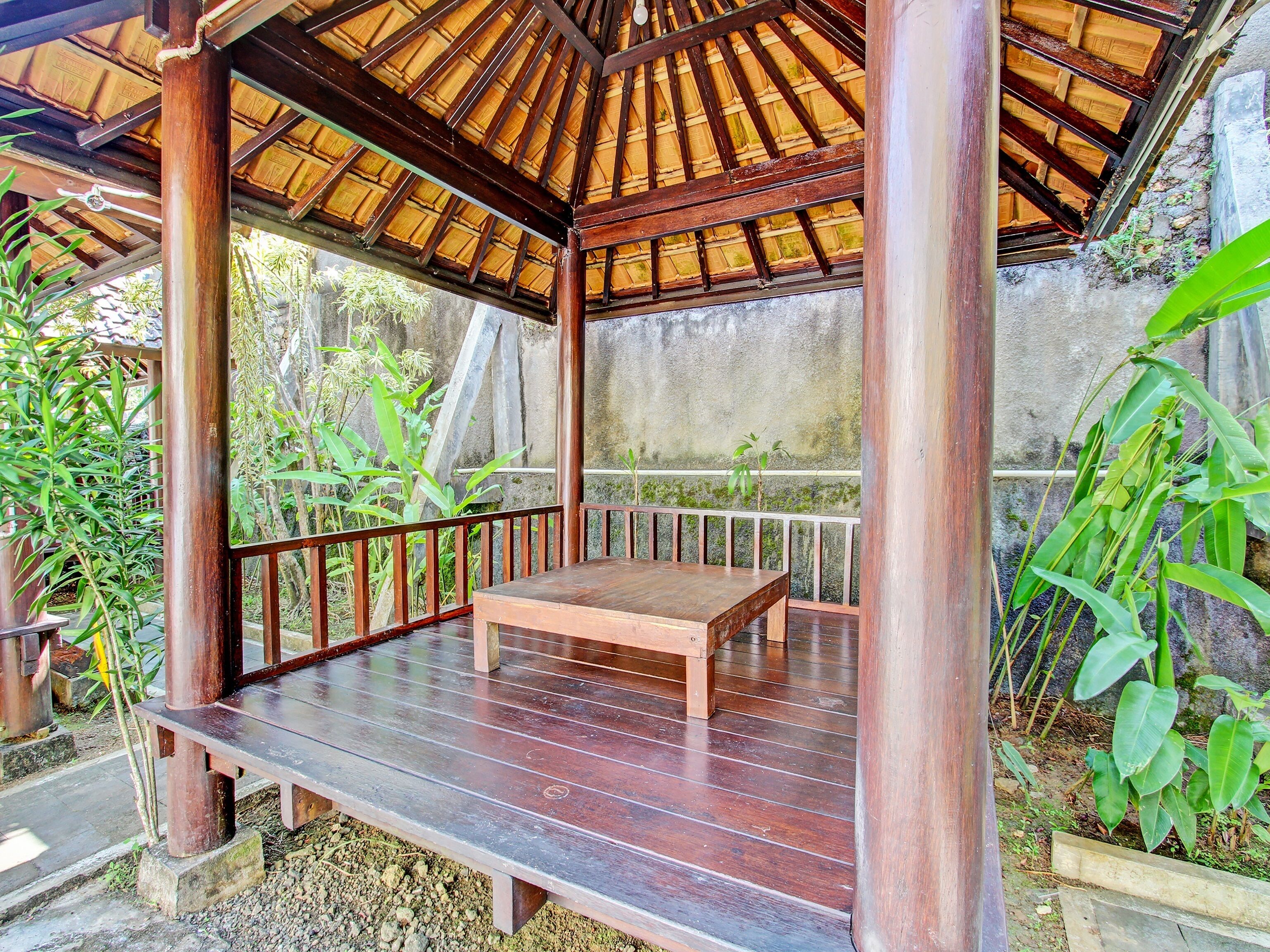 A wooden gazebo with a bench, surrounded by greenery.