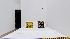 Una habitación de hotel pequeña y estrecha con una cama, dos almohadas con diseños amarillos y azules, y una colcha azul oscuro.