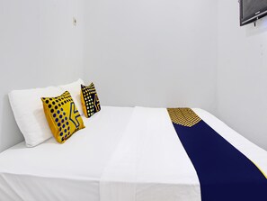 A bed with white bedding, two pillows with yellow and black patterns, and a blue and yellow geometric throw. - Hotel O Orchid Guest House (Yogyakarta)