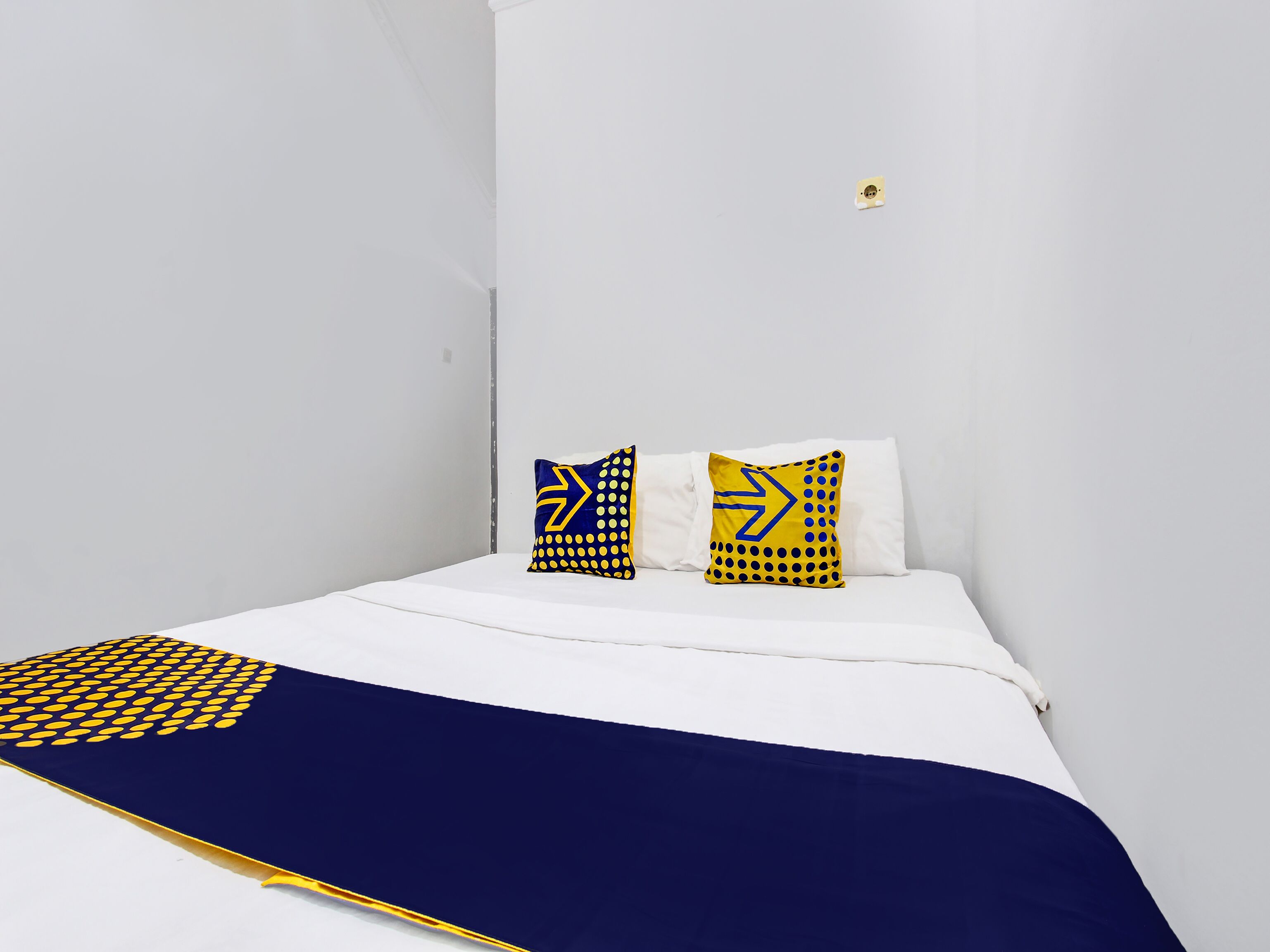 Cama com roupa de cama branca e duas almofadas decorativas com padrões geométricos.