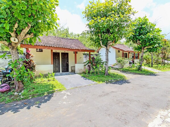 A row of small, single-story buildings with tiled roofs, surrounded by greenery and a paved driveway. - Hotel O Orchid Guest House (Yogyakarta)