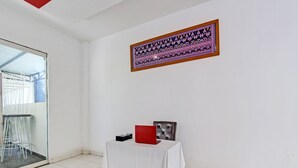 Una habitación con una mesa blanca, una obra enmarcada en la pared, y un ventanal de vidrio que da a un balcón.