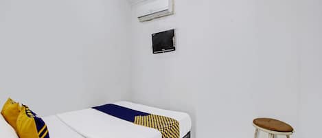 Una habitación pequeña y limpia con una cama, un taburete, un equipo de aire acondicionado y un televisor.