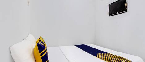 A single bed with white bedding and a blue and yellow patterned blanket. There is a white pillow and a yellow and blue pillow on the bed. An air conditioning unit is mounted on the wall above the bed.
