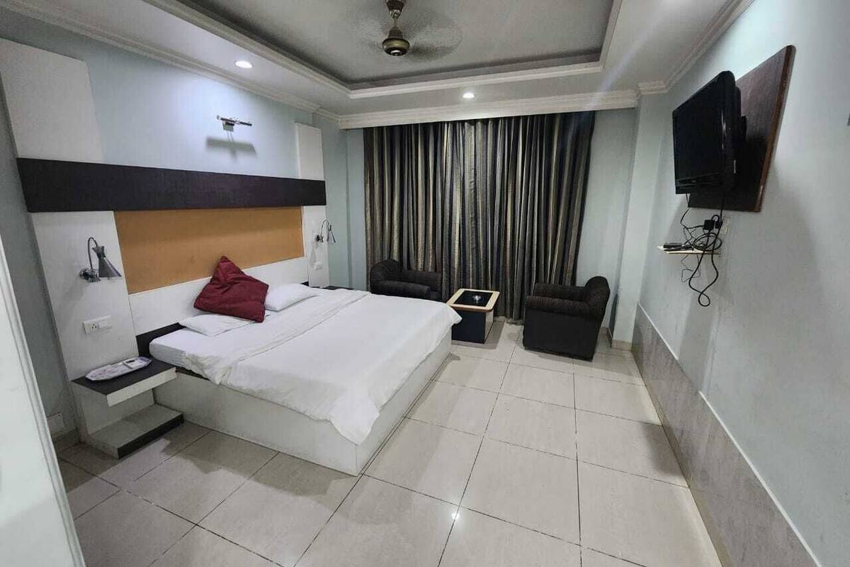 Quarto de hotel com cama, escrivaninha, cadeira, televisão e cortinas.