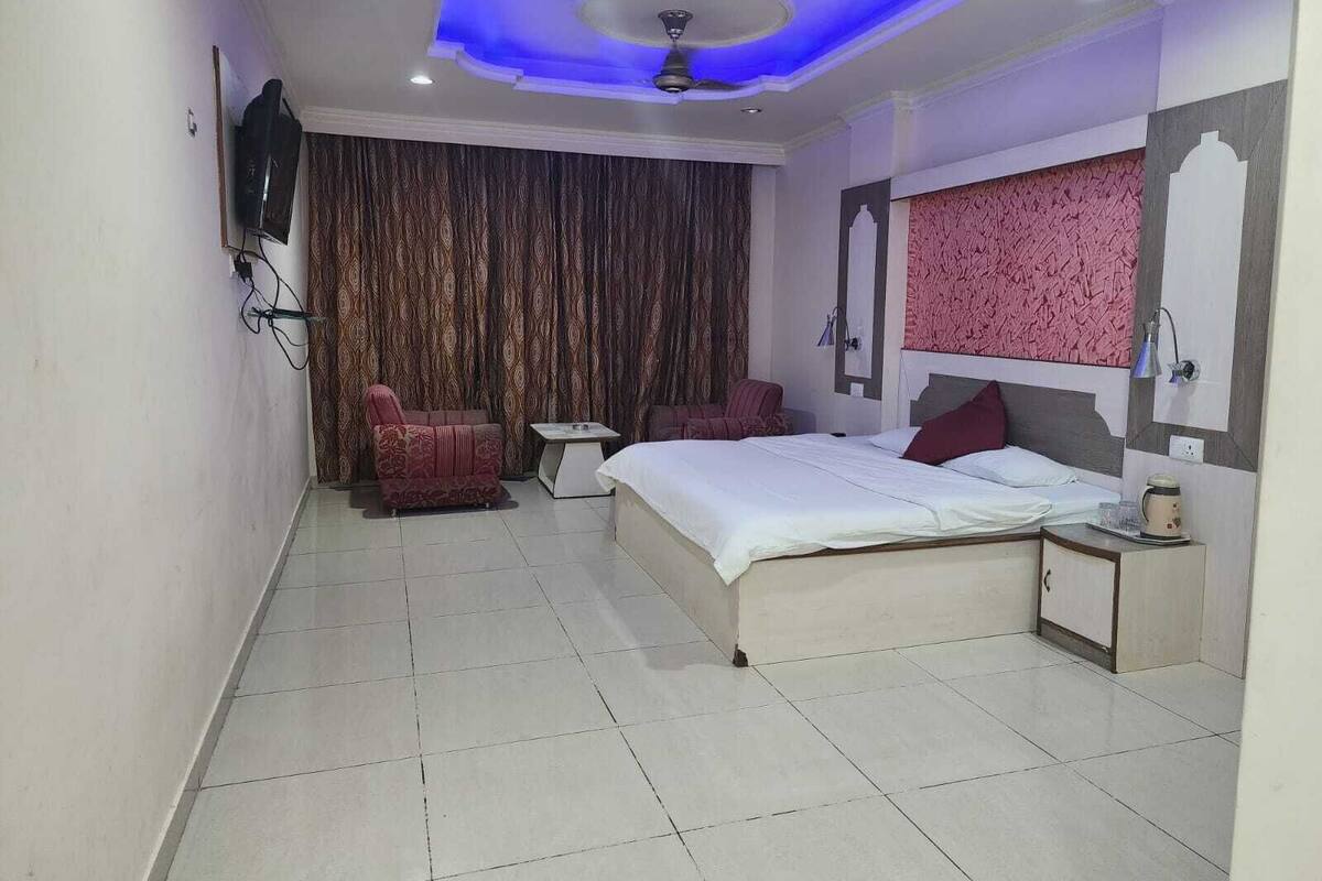 Quarto de hotel com uma cama, duas cadeiras, uma mesinha e um ventilador de teto.
