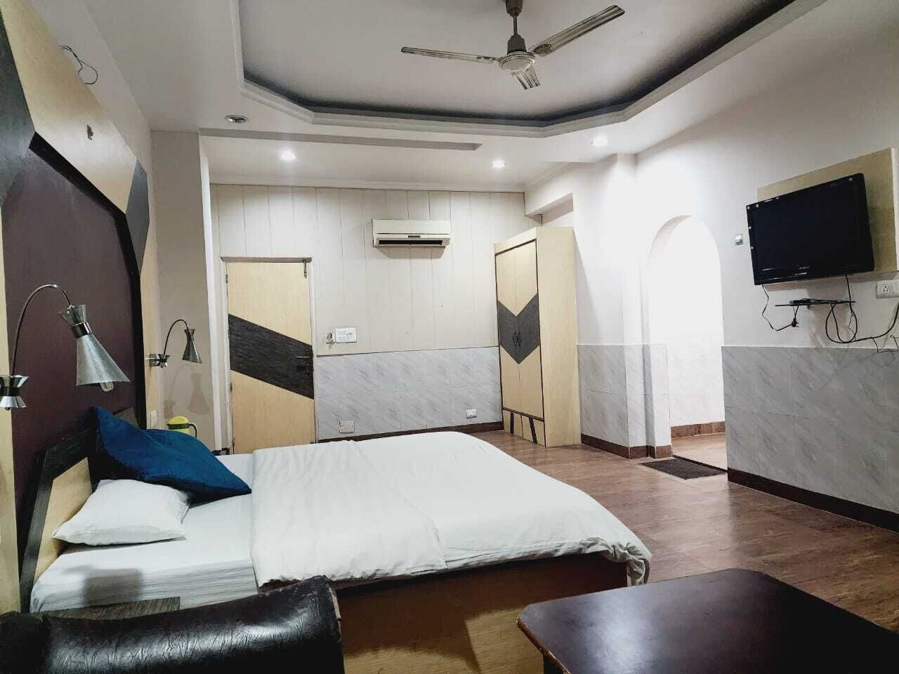 A hotel room with a bed, a desk, a TV, and an air conditioning unit.
