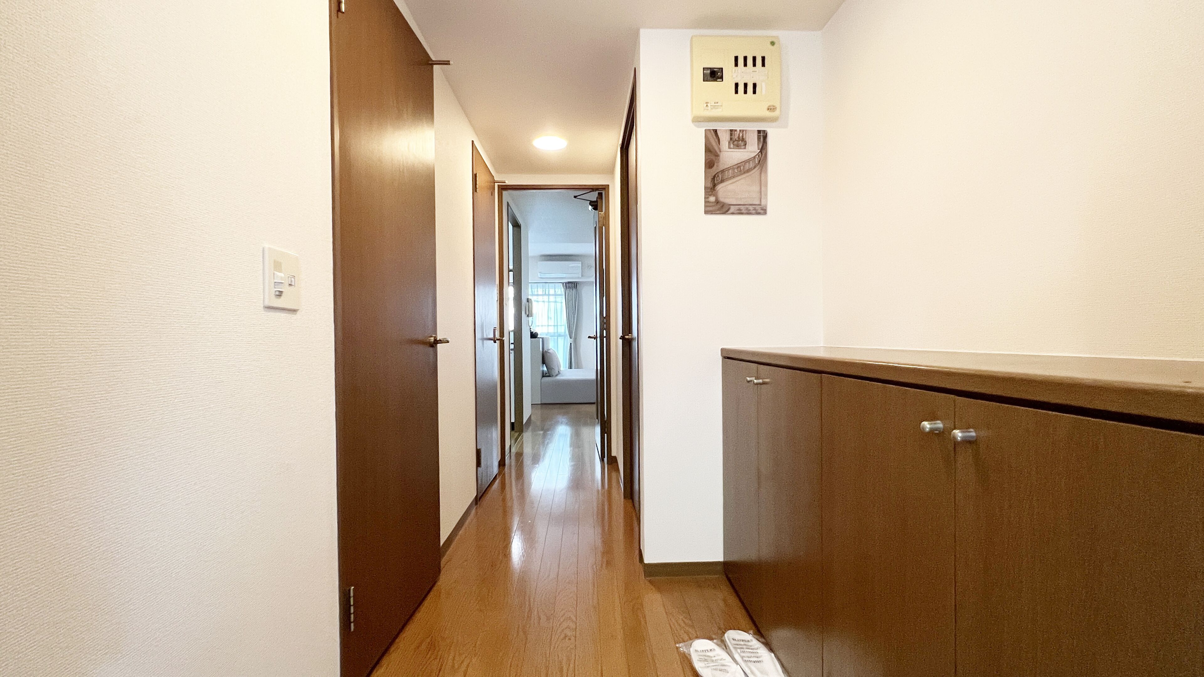 A narrow hallway with wooden flooring, a brown door on the left, and a white wall with a mounted air conditioning unit.