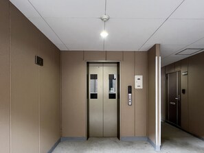 A hallway with an elevator, a fire alarm, and a door with a number plate. - Dio Higashi Shinsaibashi (Osaka)
